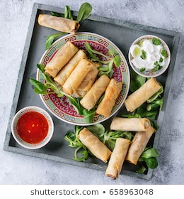 Fried spring rolls with red and white sauces, served in china plate on square wood tray with fresh green salad over gray blue texture background. Flat lay, space. Asian food. Square image