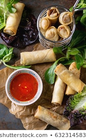 Fried spring rolls with red pepper sauce, served on crumpled paper and in fry basket with fresh green salad over old metal texture background. Top view. Asian food