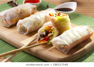 Portion of spring rolls on a bamboo board with dipping sauce
