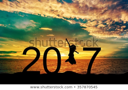 Silhouette young woman jumping on the sea and 2017 years while celebrating new year