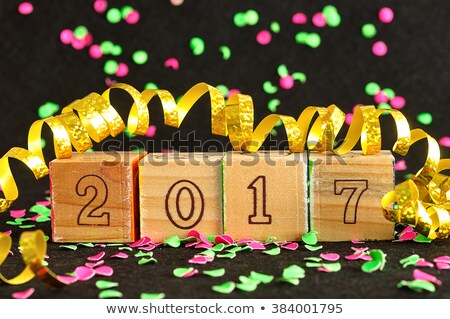2017 in wooden blocks displayed with pink and green confetti and a gold ribbon on a black background
