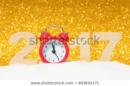 Happy new year 2017 greeting card. Alarm clock and the wooden numbers 2017 in a snowdrift on a gold glitter background